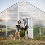 Two people working with a laptop outside greenhouse