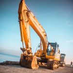 yellow excavator on gray rock near body of water during daytime